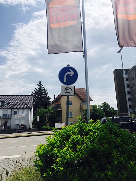 Schild "Links abbiegen" und Radfahrer von beiden Seiten