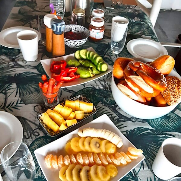 Frühstückstisch mit Obst, Brezeln und aufgeschnittener Gurke