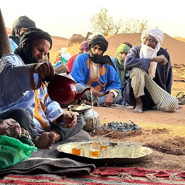 Mehrere Mönner in der Wüste vor einem Zelt bei der Teezeremonie. 