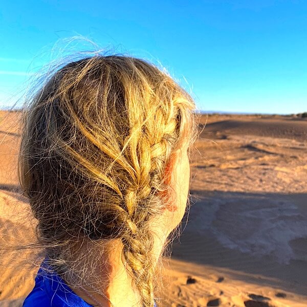 Frau mit Zopf schaut in die Wüste. 