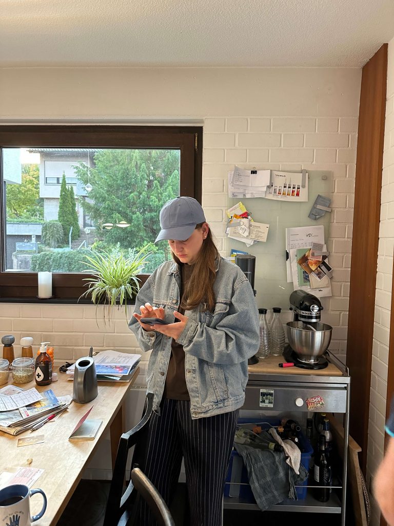 Frau mit Kappe steht in einem Zimmer mit Tisch und Pinnwand