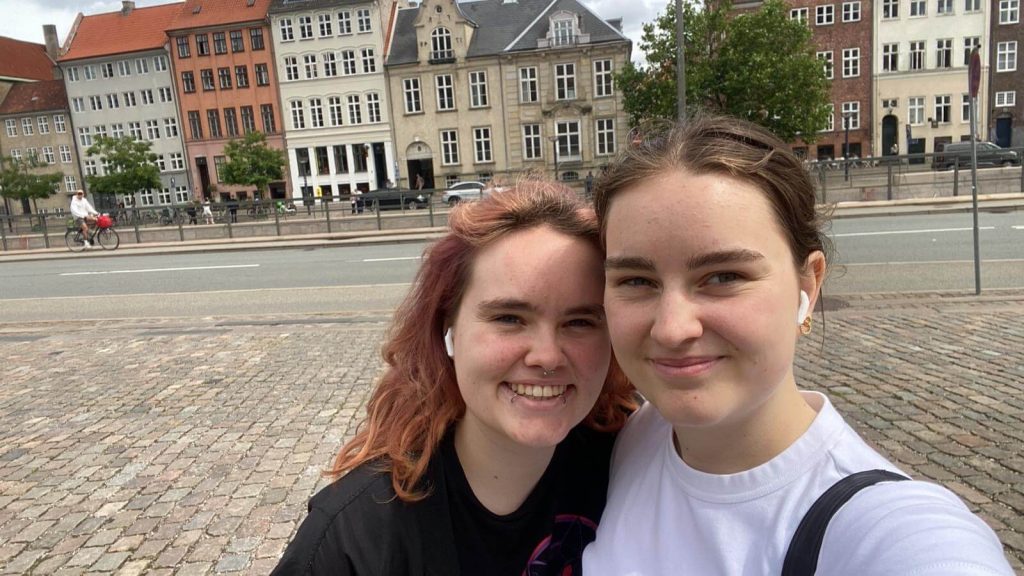 zwei junge Frauen stehen vor großem Haus auf Straße