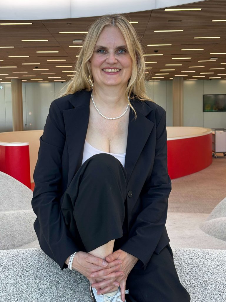 Frau im schwarzen Businessoutfit sitzt mit angezogenem Knie