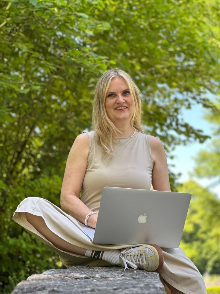 Frau sitzt im Schneidersitz mit Laptop vor einem Baum