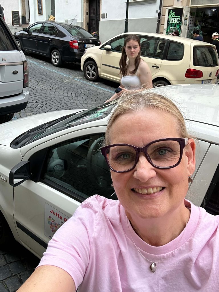 Frau steht vor Auto und lacht.