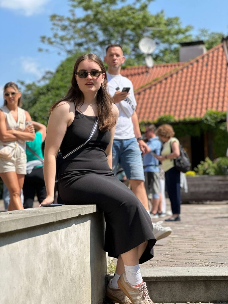Frau sitzt auf Mauer und lächelt in die Kamera.