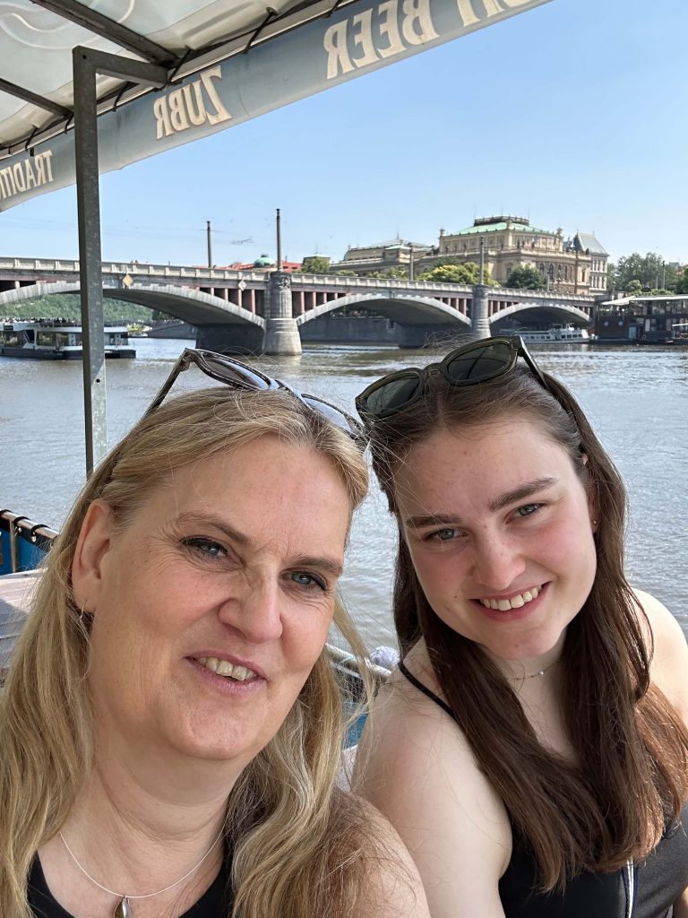 Zwei Frauen lächeln in die Kamera. Im Hintergrund eine Brücke.