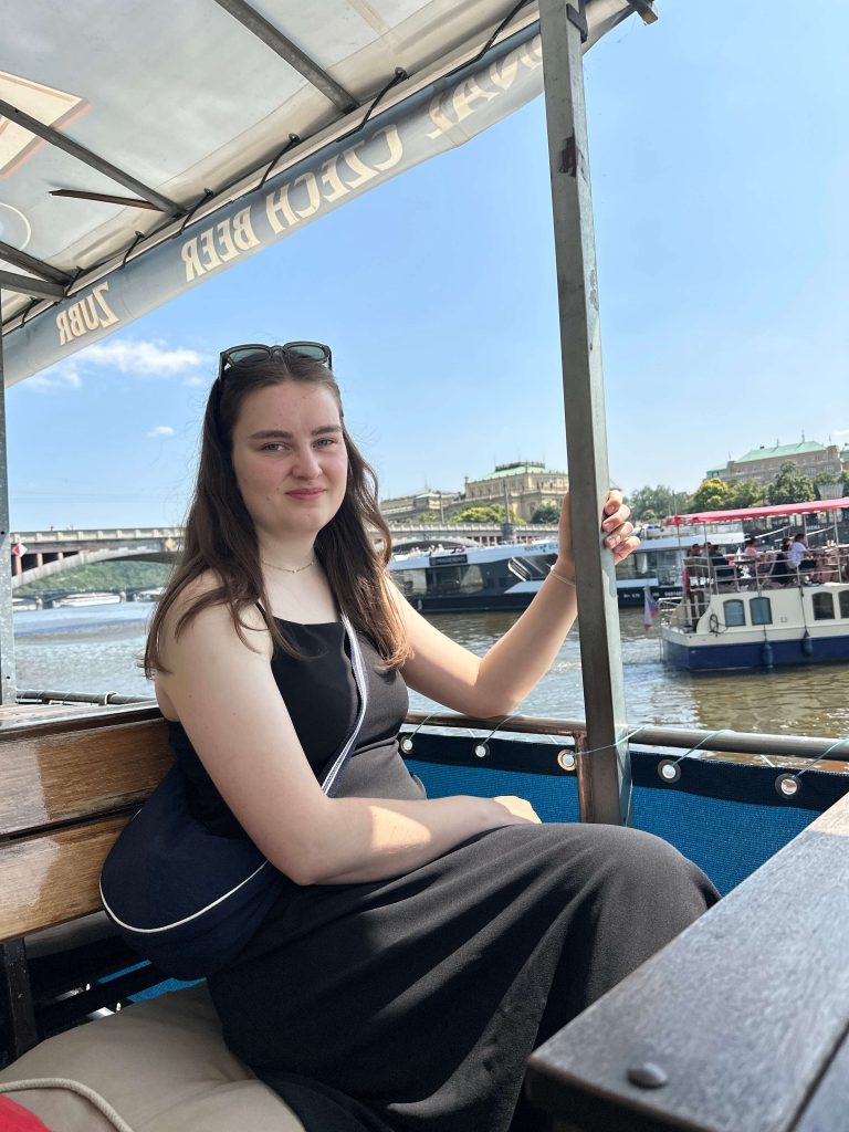 Frau auf Boot lächelt in die Kamera. Sie hält sich an einem Pfosten fest.