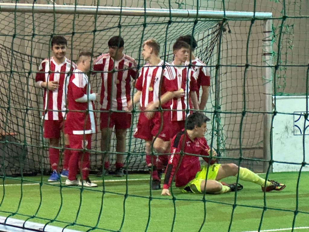 Im Vordergrund ist ein Tornetz zu sehen. Dahinter eine Mannschaft Fußballspieler, die für ein Foto aufgestellt sind