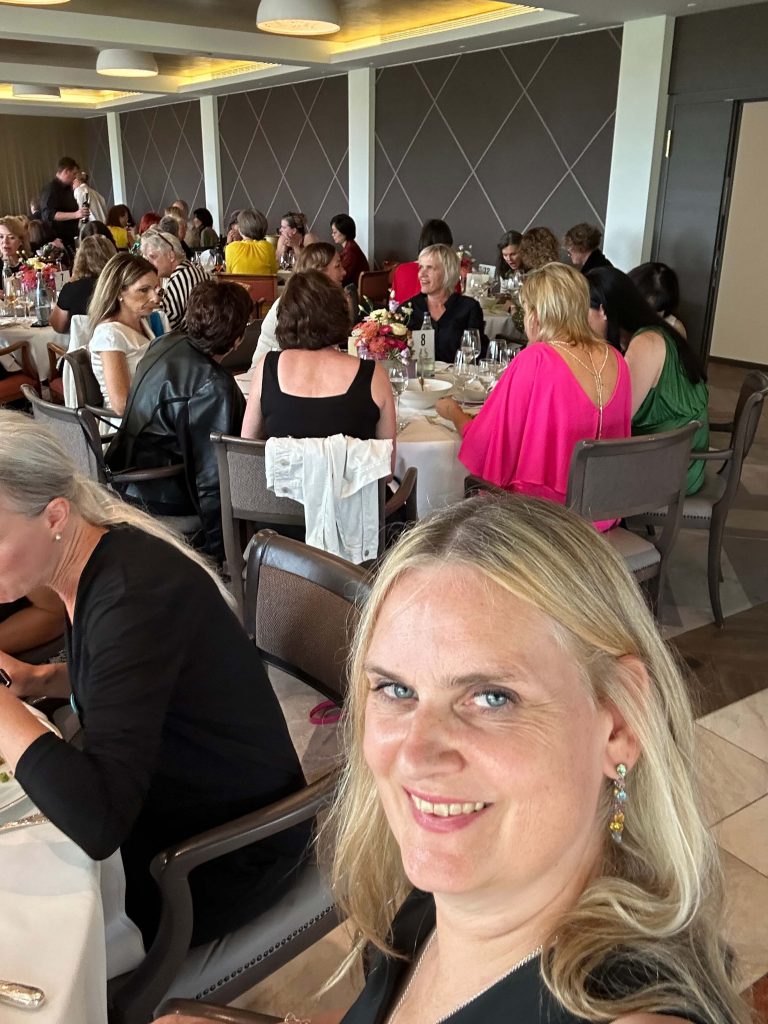 Jutta Büttner lacht in die Kamera. Im Hintergrund Frauen, die einen Vortrag hören.