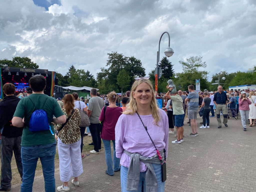 Frau lacht in die Kamera. Im Hintergrund viele Menschen.