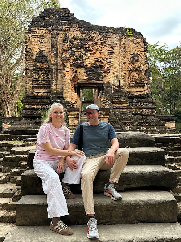 Ein Mann und eine Frau sitzen auf einer Treppe vor einer Ruine eines Tempels in Kompont Thom