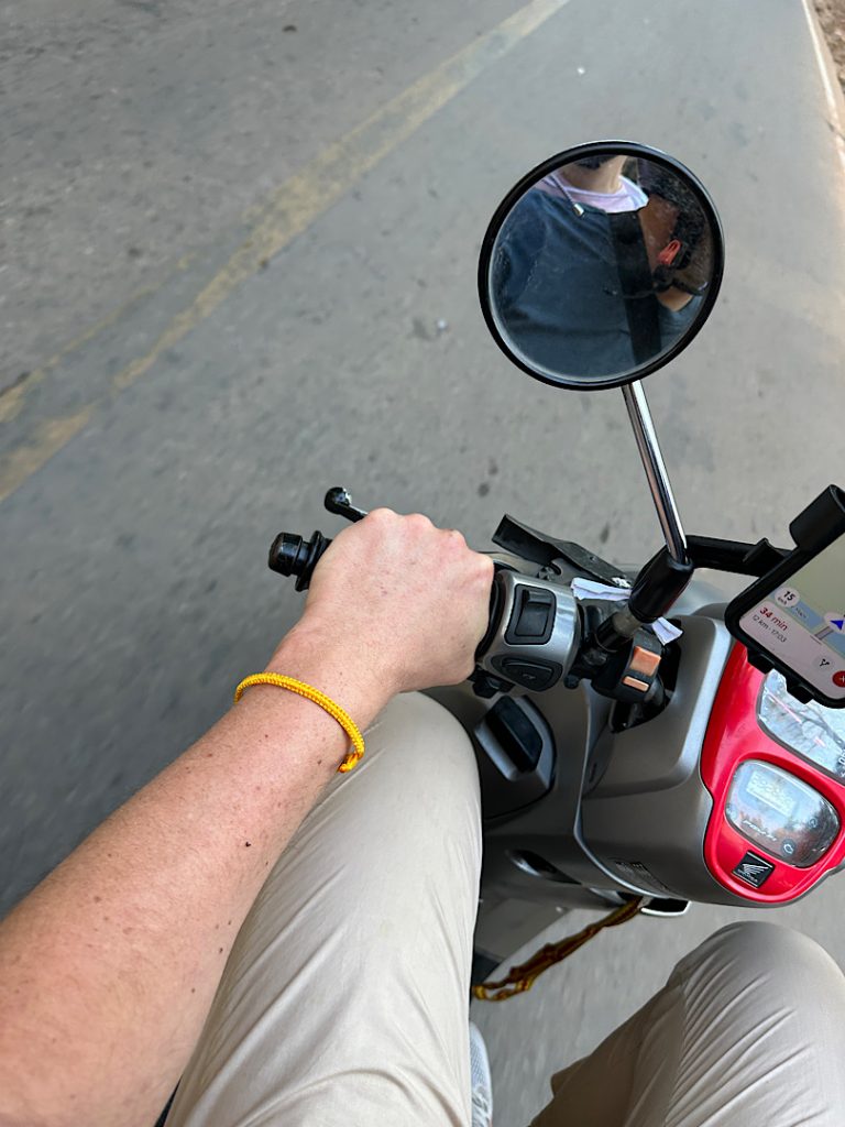 Man sieht das Lenkrad eines Motorrads. Man sieht den linken Arm eines Mannes. Er trägt ein gelbes Armband.