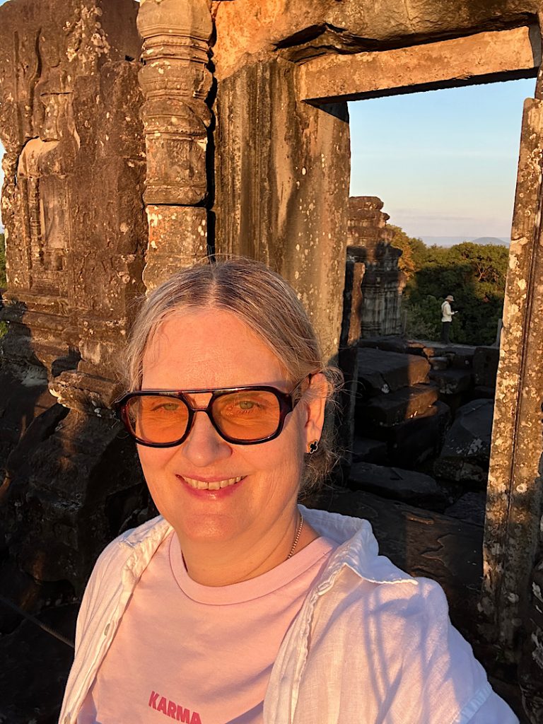 Eine Frau mit Sonnenbrille steht vor einem Tempelrest auf dem Berg Phnom Bakheng, Angkor Wat, Siam Reap, Kambodscha