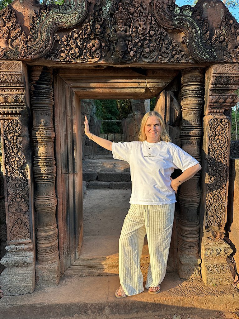 Eine Frau in weißem Shirt und weißen Hosen posiert vor einer Türöffnung in Angkor Wat, Kambodscha