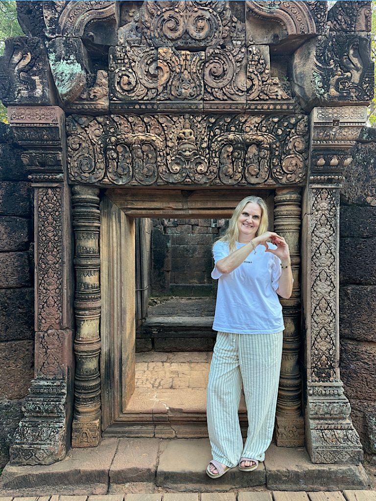 Eine Frau in grauem Shirt und weißen Hosen posiert vor einer Türöffnung in Angkor Wat, Kambodscha