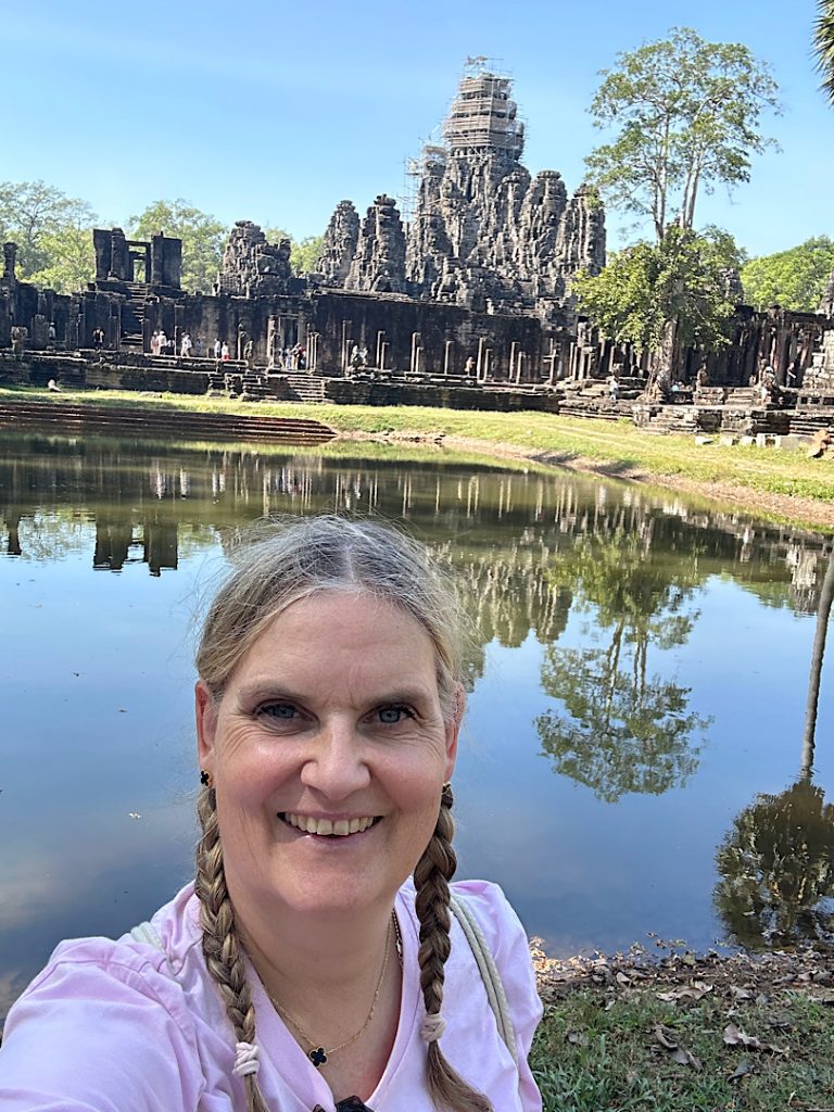 Eine Frau lacht in die Kamera. Im Hintergrund ist Angkor Thom, Kambodscha, Siam Reap zu sehen