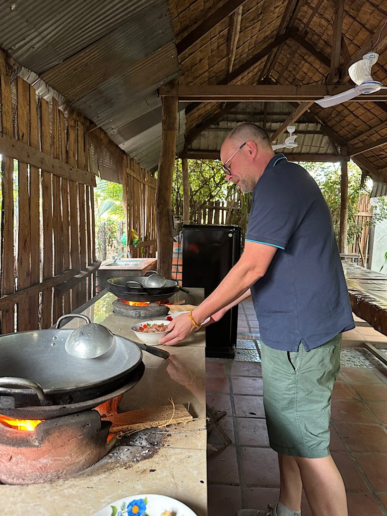 Europäischer Mann steht an einem Herd in Kambodscha, der noch mit Holz befeuert wird.