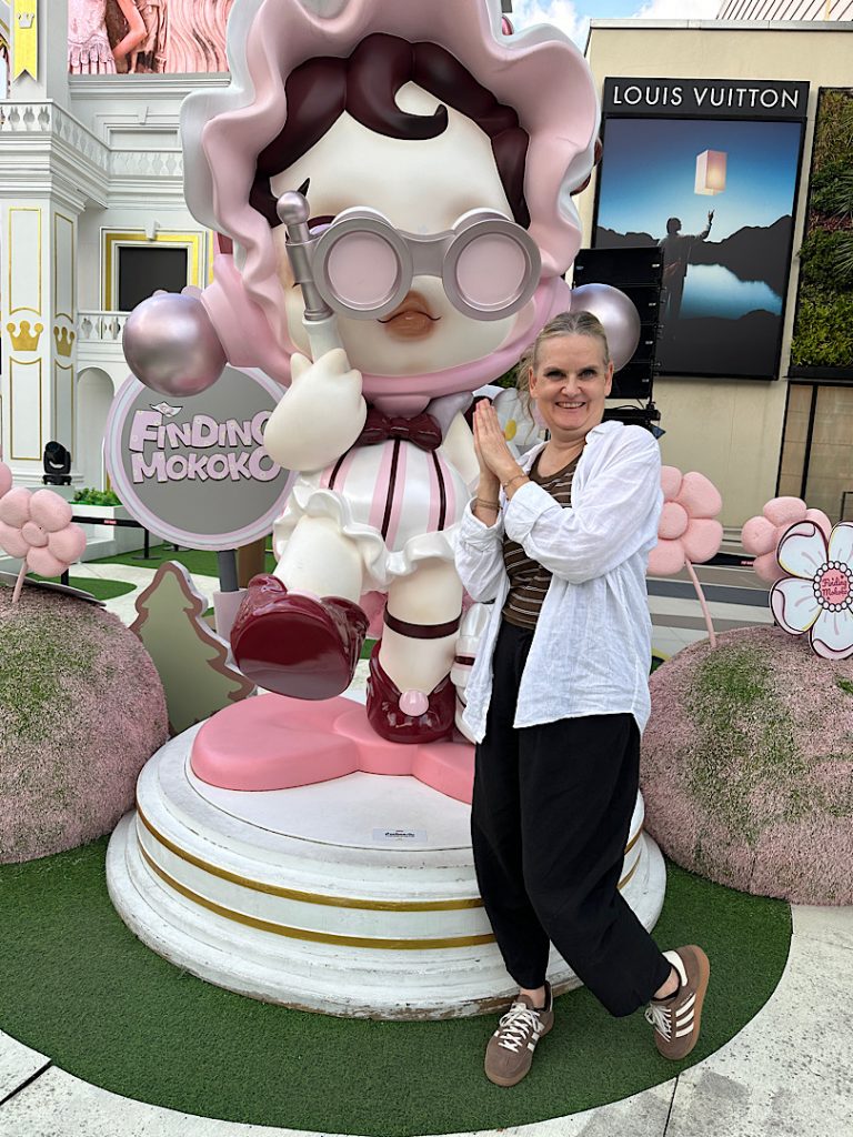 Frau steht vor einer großen Figur und lacht in die Kamera