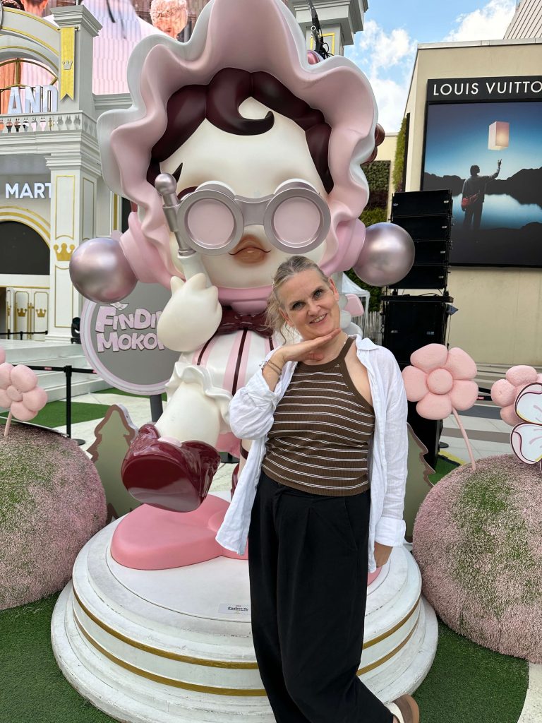 Frau steht vor einer großen Plastikfigur und lacht in die Kamera