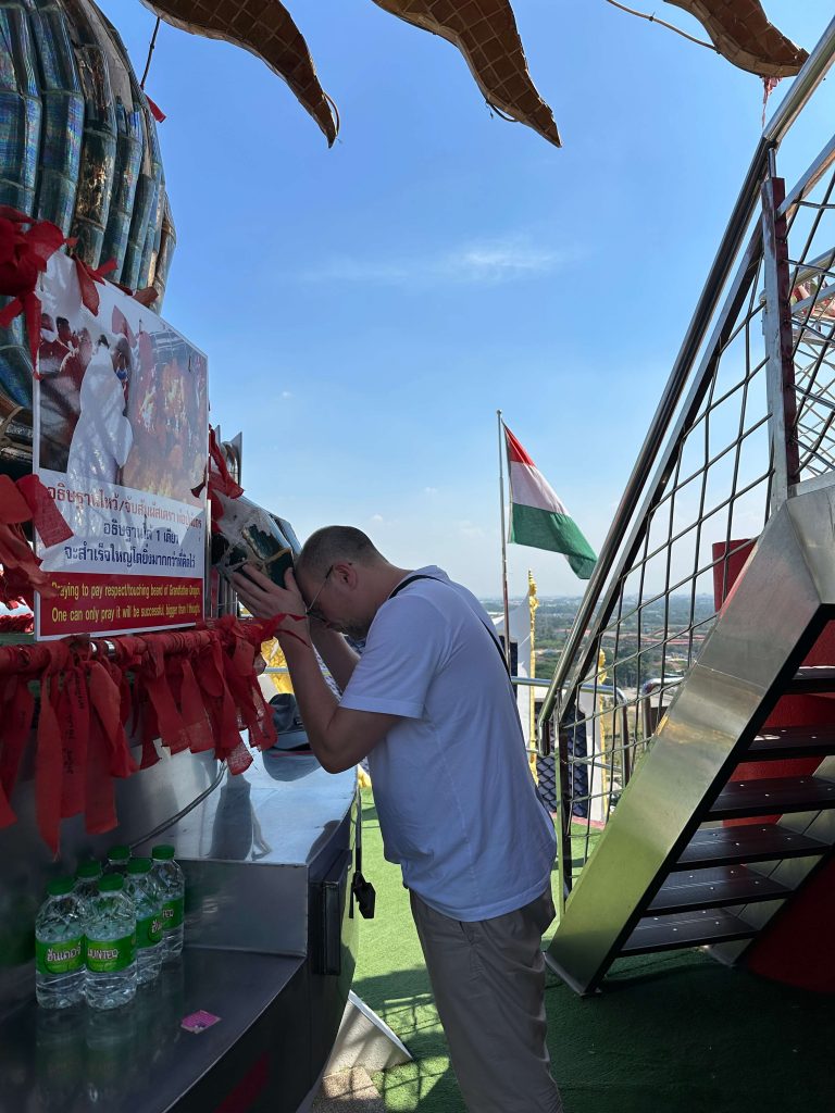 Ein Mann berührt mit seiner Stirn die Zunge eines Drachens. Rechts ist eine Stahltreppe zu sehen.