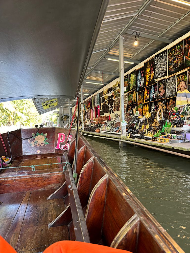 Links ist ein Teil des Bootes zu sehen, auf dem sich der Fotograf befindet. Rechts ist ein Marktstand zu sehen, der mit dem Boot erreicht werden kann.