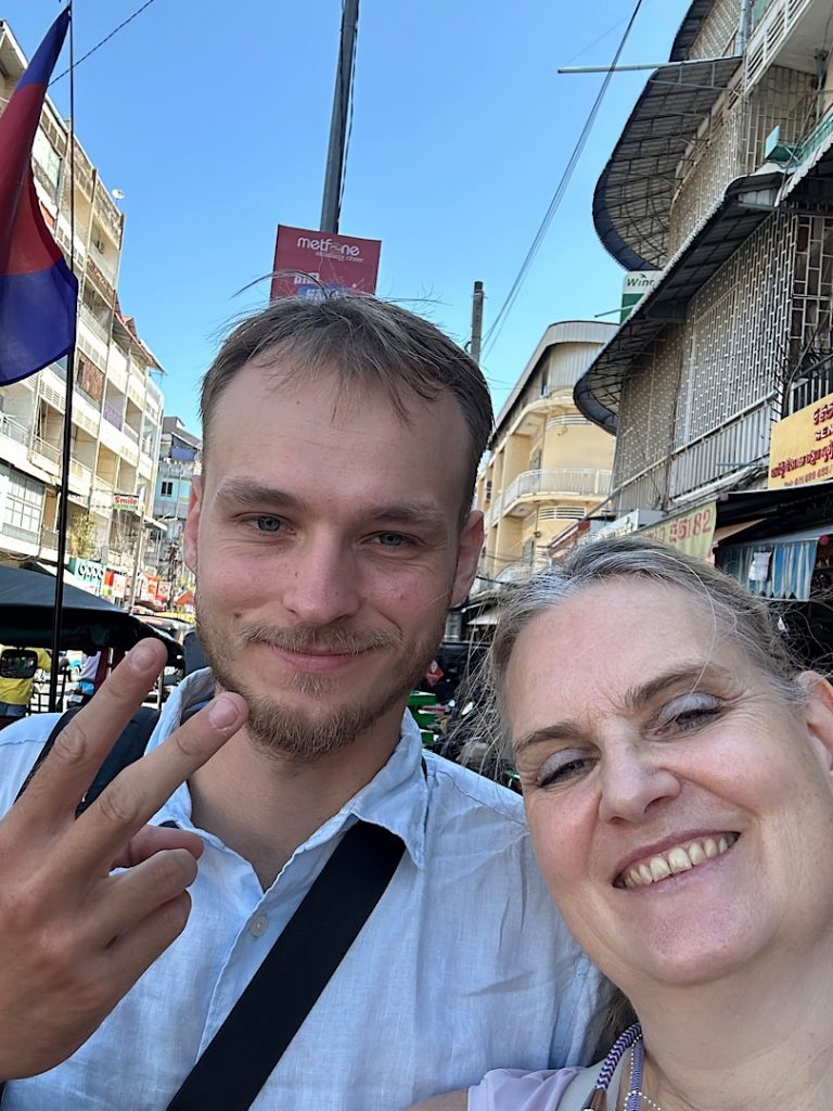 Eine Frau und ein Mann lachen in die Kamera für ein Selfie. Im Hintergrund der Markt in Phnom Penh Kambodscha