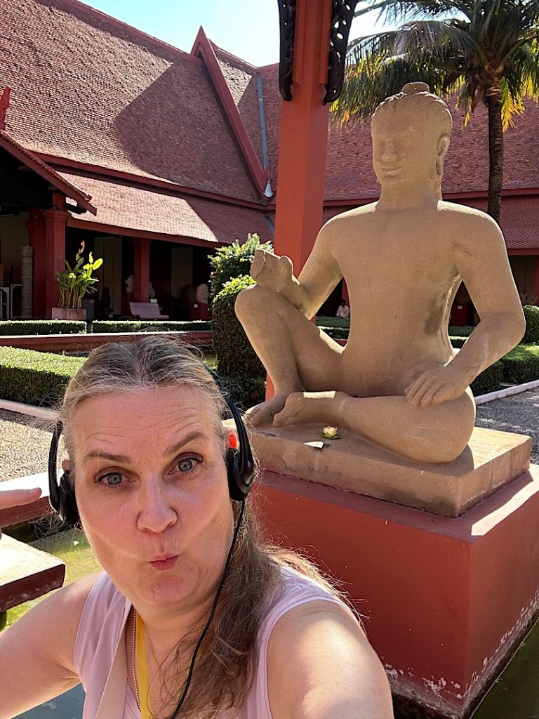 Eine Frau mit Kopfhörern spitzt die Lippen. Sie sitzt vor einer Buddha-Statue im Nationalmuseum Kambodscha, Phnom Penh.