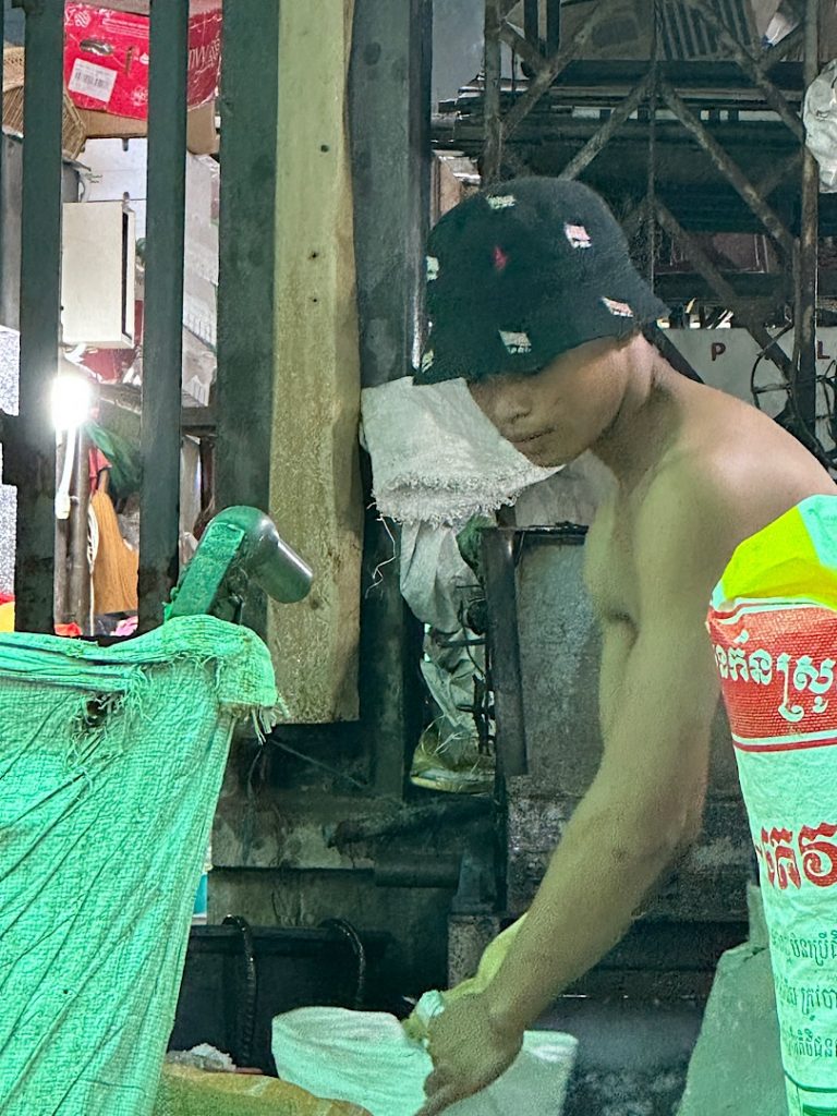 Junger Mann mit nacktem Oberkörper. Er trägt eine Mütze. Er zerkleinert einen Eisblock