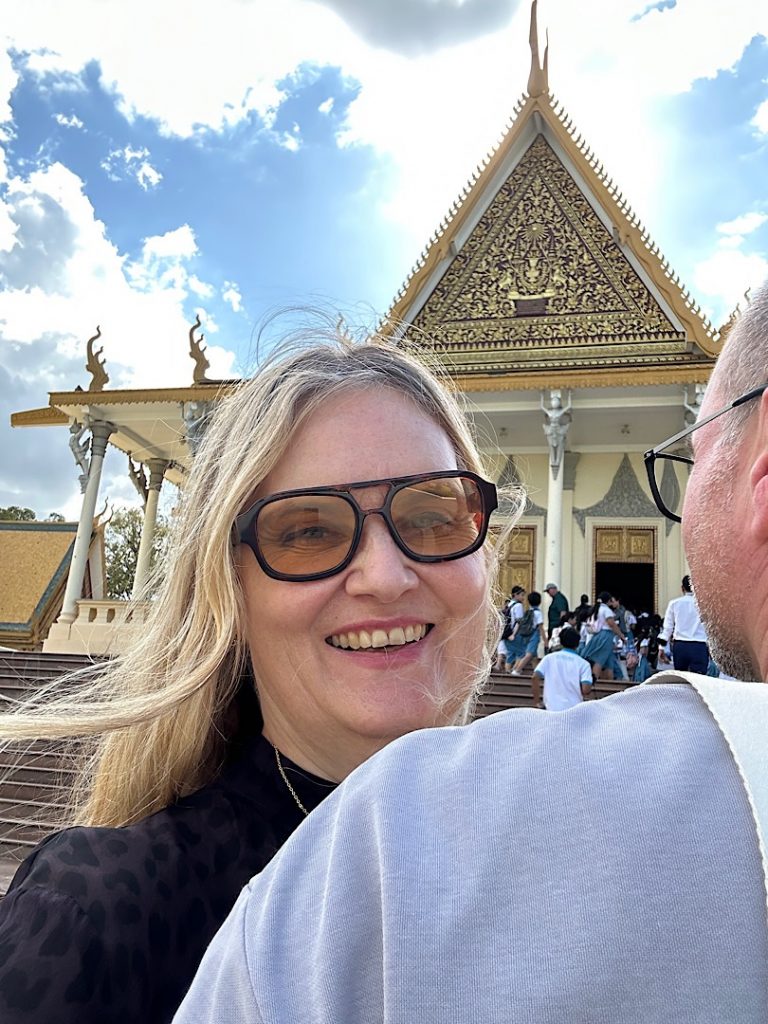 Eine Frau lächelt über die Schulter eines Mannes. Im Hintergrund ist ein Gebäude im Khmerstil zu sehen.