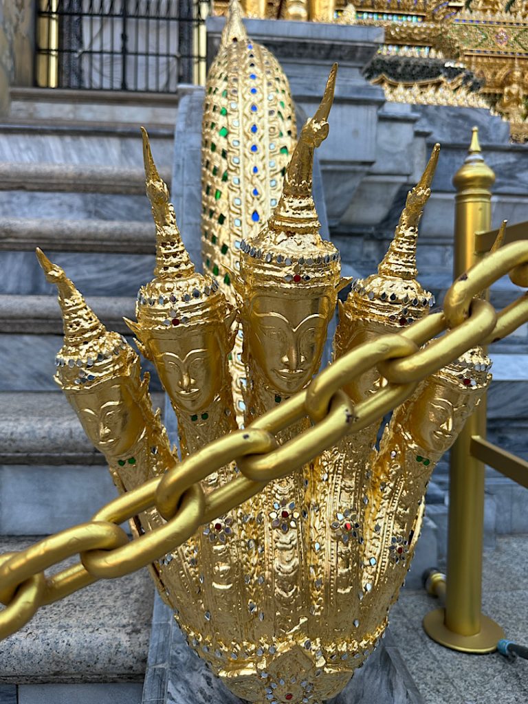 Im Vordergrund ist eine goldene Kette. Dahinter fünf Köpfe einer goldenen Schlange