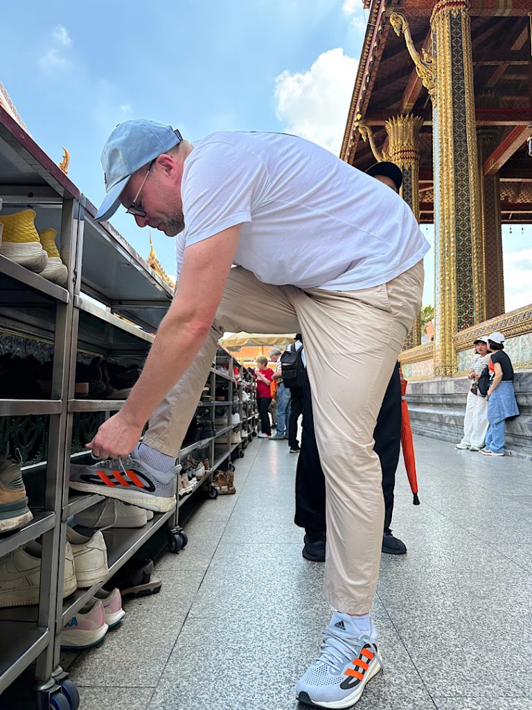 Mann steht an einem Schuhregal vor einem buddisthischen Tempel und bindet seine Schuhe