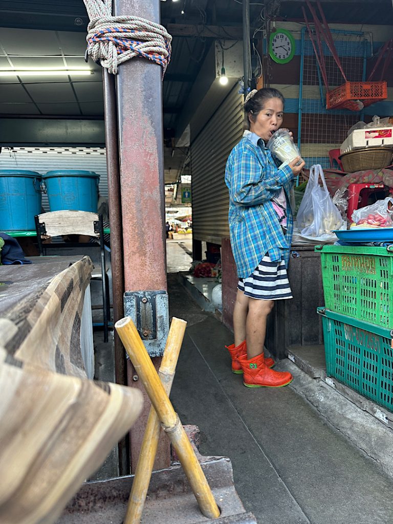 Frau steht in einem Marktstand in Thailand. In der Hand hält sie einen Shake