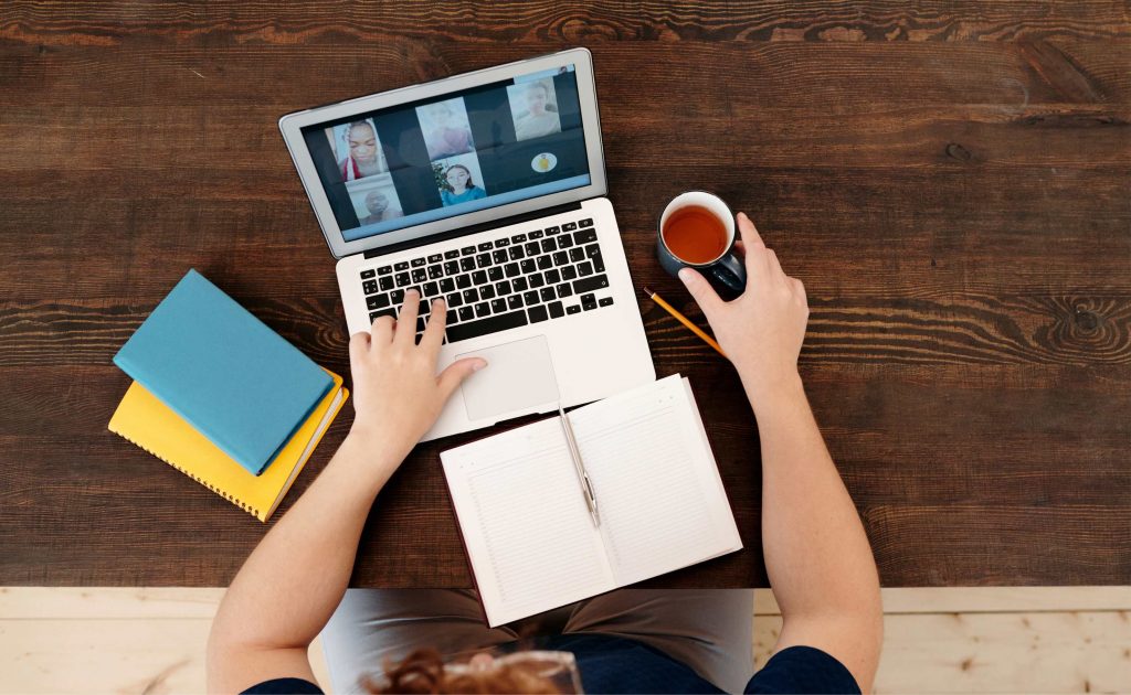 Die Kamera ist an der Decke befestigt und fotografiert den Schreibtisch. Darauf ist ein Laptop, ein aufgeschlagenes Buch und die Arme einer Person zu sehen. Sie tippt auf der Tastatur mit einer Hand. In der anderen Hand hält sie eine Teetasse.