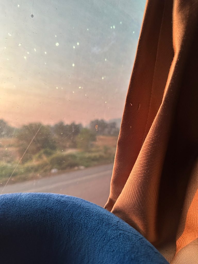 Blick aus einem Fenster auf die Straße. Am rechten Rand ist ein oranger Vorhang zu sehen.