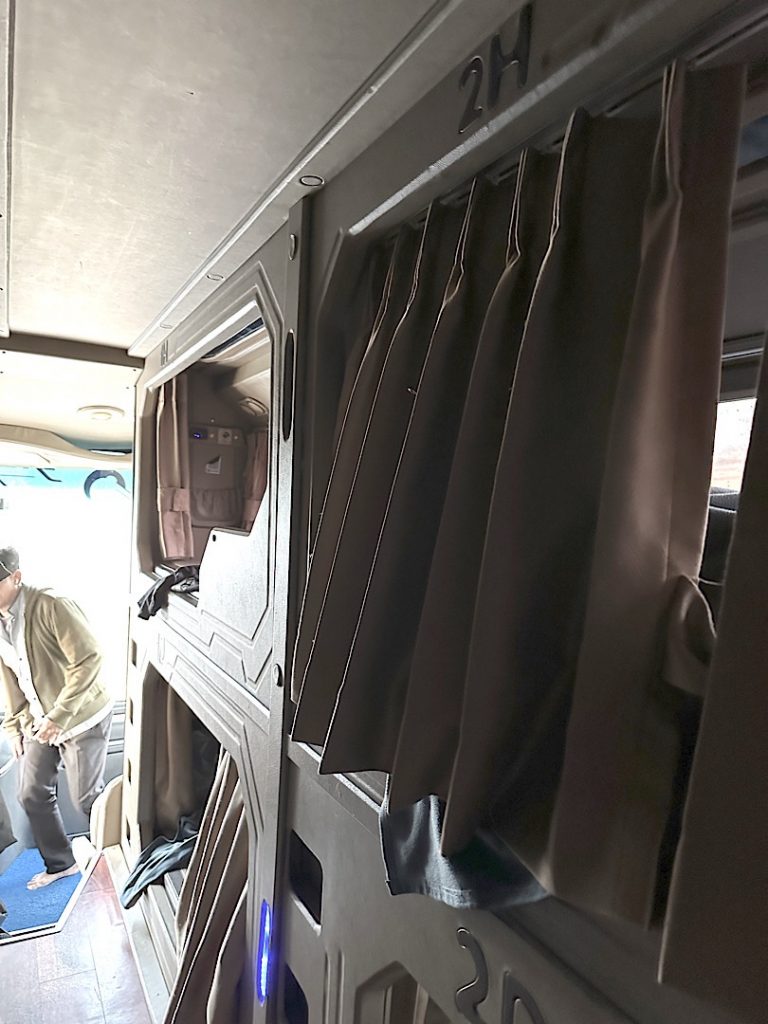 Der Gang eines Nachtbusses ist zu sehen. Der Vorhang der Kabine ist zugezogen.